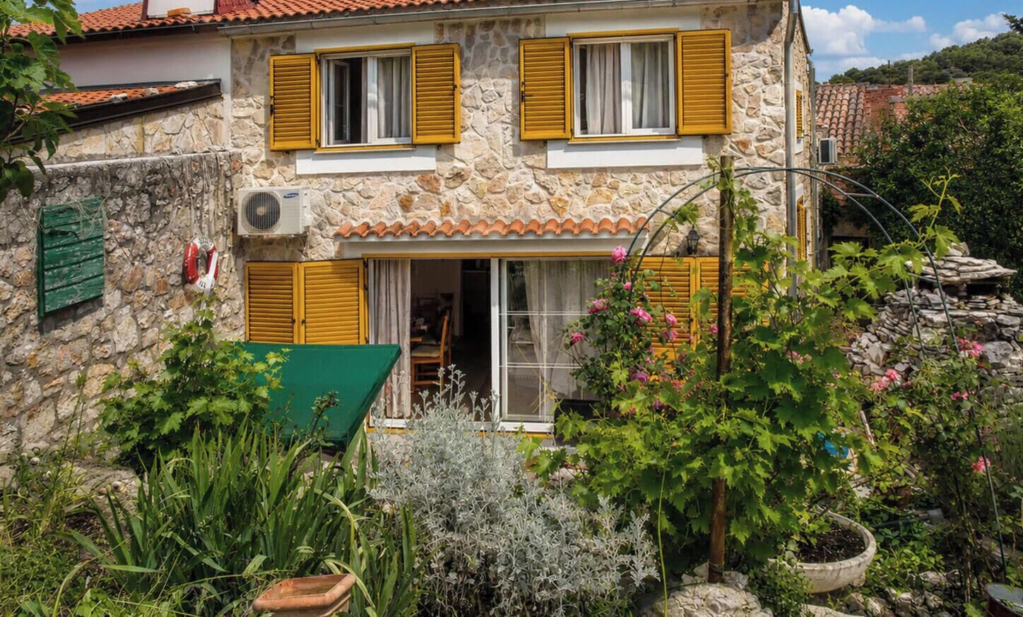 A stone building with a tiled roof, a wooden door, and a window with yellow shutters.