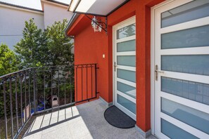 A red exterior wall with a glass door and a small balcony with a metal railing. - Apartment Blue Harmony (Crikvenica)