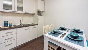 Et moderne køkken med hvide skabe, en mikrobølgeovn og et spisebord dækket med blå tallerkener og glas.