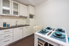 A modern kitchen with white cabinets, a microwave, and a dining table set with blue plates and glasses. - Apartment Blue Harmony (Crikvenica)