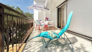A balcony with a table and chairs, a striped umbrella, and a blue sun lounger. - Apartment More (Vodice)