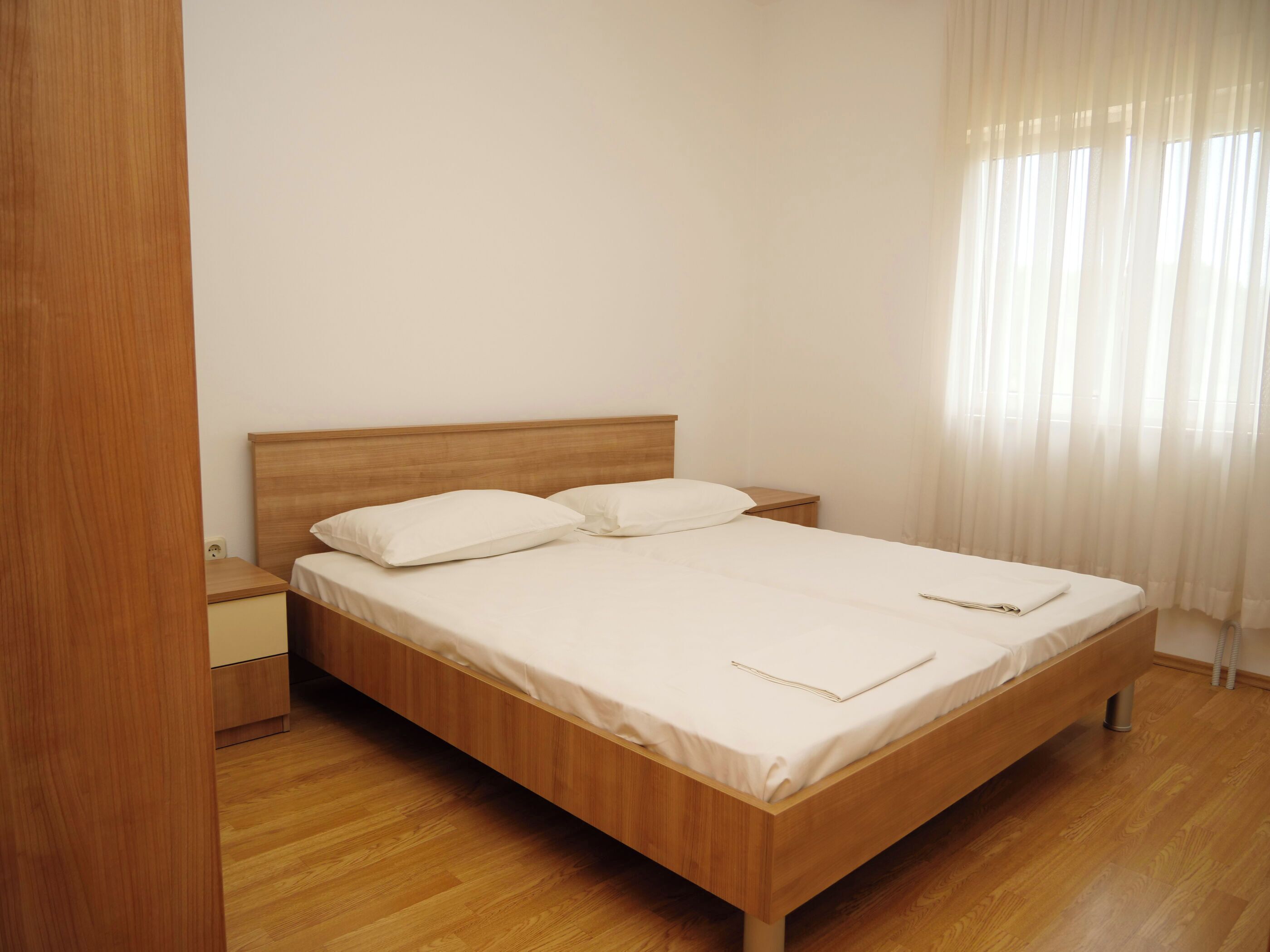 A bedroom with a wooden bed, white bedding, and a nightstand.