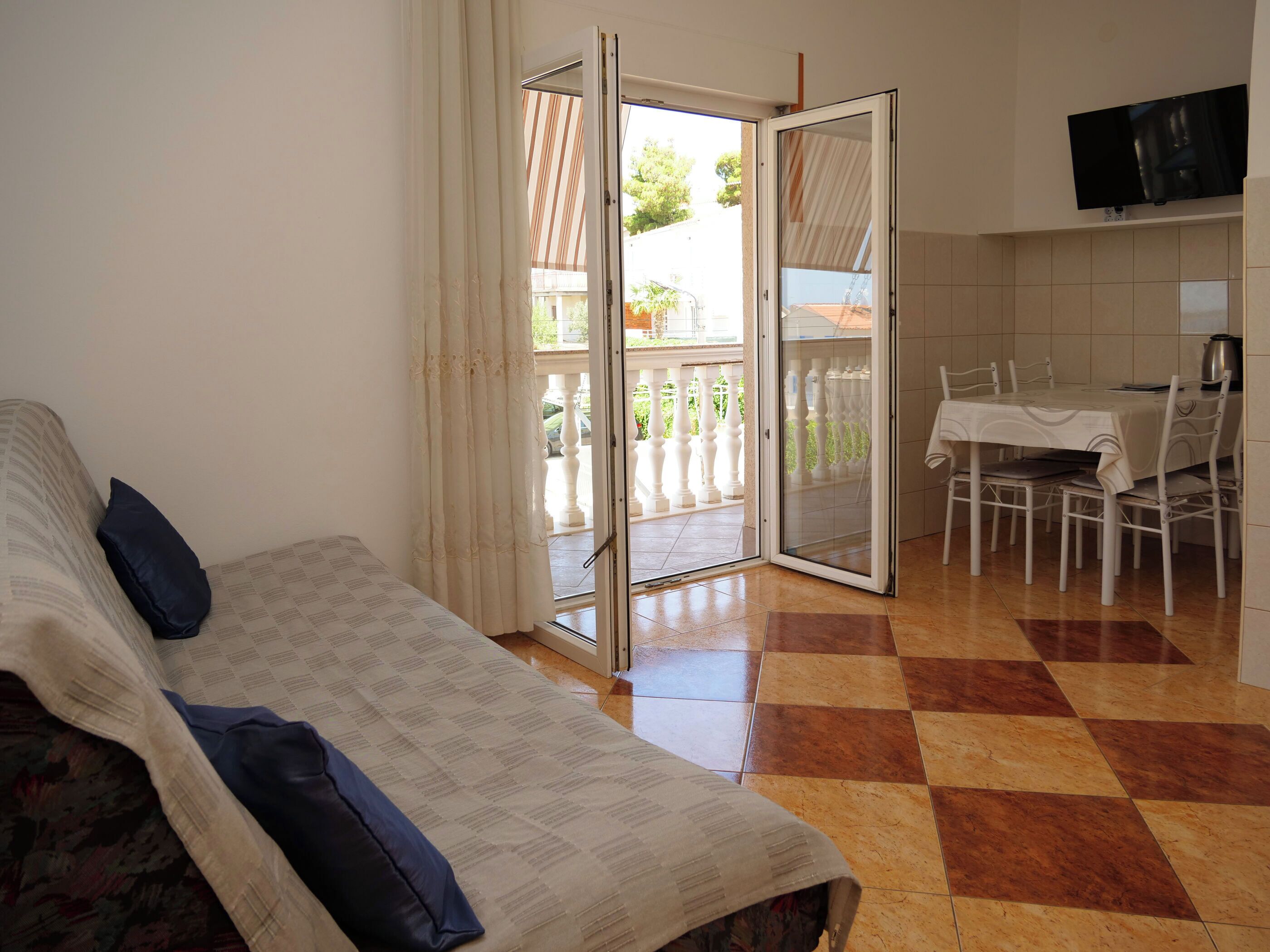 Quarto com sofá, mesa de jantar com cadeiras, televisão na parede e porta de vidro deslizante para área externa.