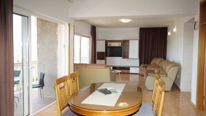 A dining area with a round table and chairs, a sofa, a television, and a sliding glass door leading to an outdoor area. - Apartments Vlade (Primosten)