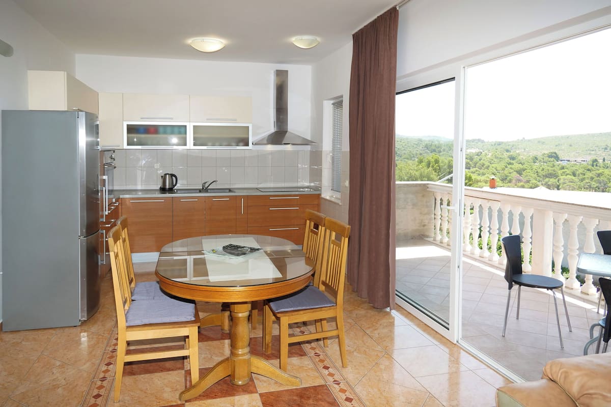 A modern kitchen with a dining area, a balcony with a view, and a large window.
