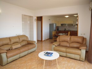 Ein Wohnzimmer mit zwei Ledersofas, einem kleinen weißen Tisch mit Zeitschriften und einer Küche im Hintergrund.