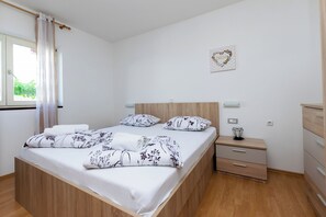 A neatly made bed with floral bedding, a bedside table with a lamp, and a wall-mounted artwork. - Apartments Miranda (Lopar)