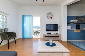 A modern living room with a television, a dining table, and a kitchen area with blue cabinets. - Apartments Miranda (Lopar)