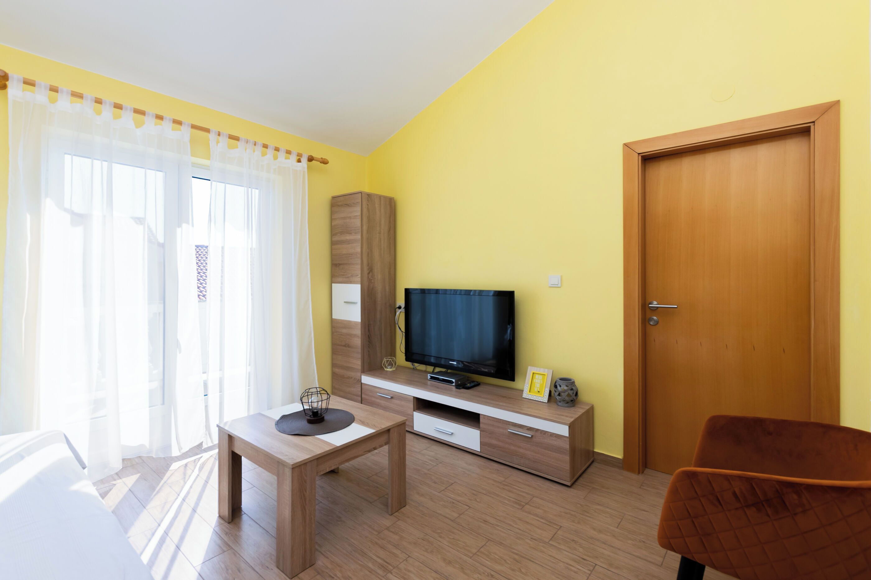 A room with a wooden TV stand, a television, a wooden cabinet, a small table, and a door.