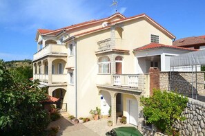 Un edificio de varios pisos con balcones, fachada de piedra y un jardín con plantas en macetas.