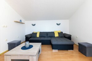 A modern living room with a sectional sofa, a small table, and a bench. - Apartments Miranda (Lopar)