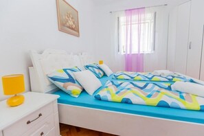 A bedroom with a bed, a bedside table, a lamp, a window with curtains, and a wardrobe. - Apartment Roko in Center (Split)