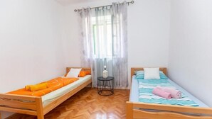 Ein Zimmer mit zwei Holzbett, einem kleinen runden Tisch und einem Fenster mit durchsichtigen Vorhängen.