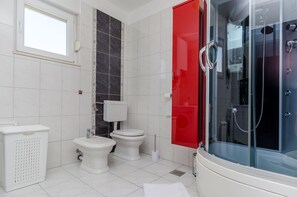 A modern bathroom with a glass-enclosed shower, two toilets, a bidet, and a white sink. - Apartment Skoko (Split)