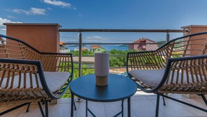 Ein Balkon mit Korbstühlen und einem Tisch, der einen schönen Blick auf ein Gewässer und entfernte Gebäude bietet.