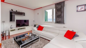Un salon moderne avec un canapé blanc, des coussins rouges, un téléviseur à écran plat et une table basse en verre.