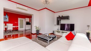 Un salon moderne avec un canapé blanc, une table basse en verre et un mur d’accent rouge.