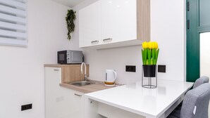 Une cuisine moderne avec des meubles blancs, un four à micro-ondes, une bouilloire et un vase rempli de fleurs jaunes posé sur le comptoir.