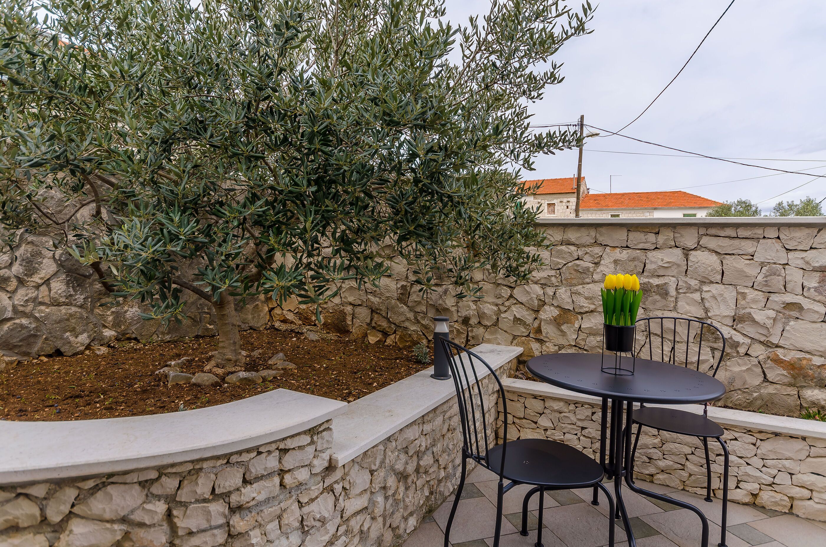 Un espace extérieur aménagé avec un mur en pierre, une table entourée de chaises et un pot de fleurs contenant des fleurs jaunes.