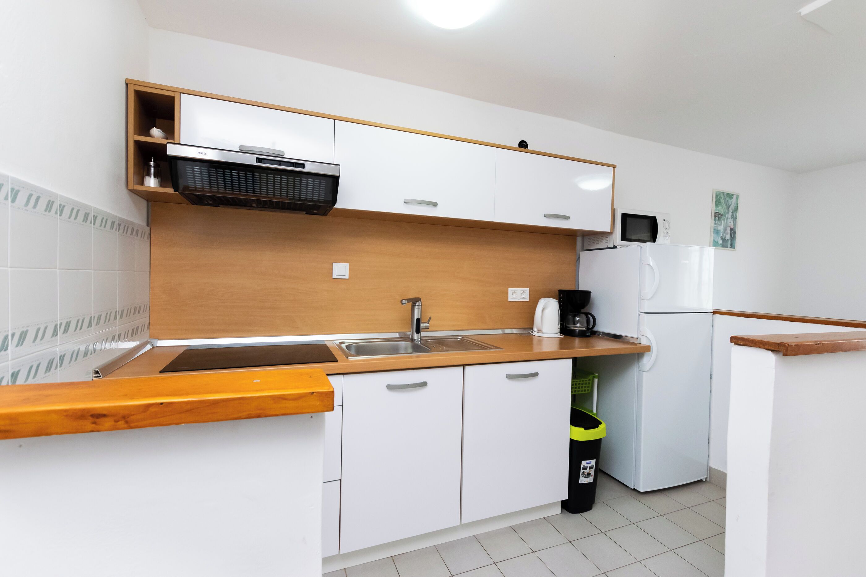 A compact kitchen with white cabinets, a wooden countertop, a sink, a microwave, a coffee maker, and a refrigerator.