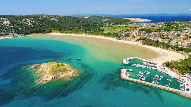 An aerial view of a coastal area with a marina, sandy beach, and residential buildings. - Apartments Milena (Lopar)