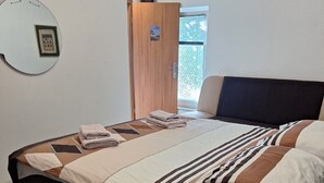 Un dormitorio moderno con una cama, un espejo redondo, una puerta de madera y una ventana.