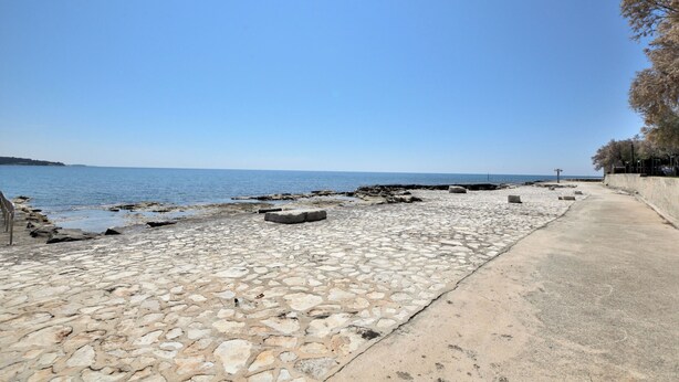 Un paseo marítimo con un sendero de piedra que conduce al mar, un camino de hormigón al lado y una vista despejada del océano.