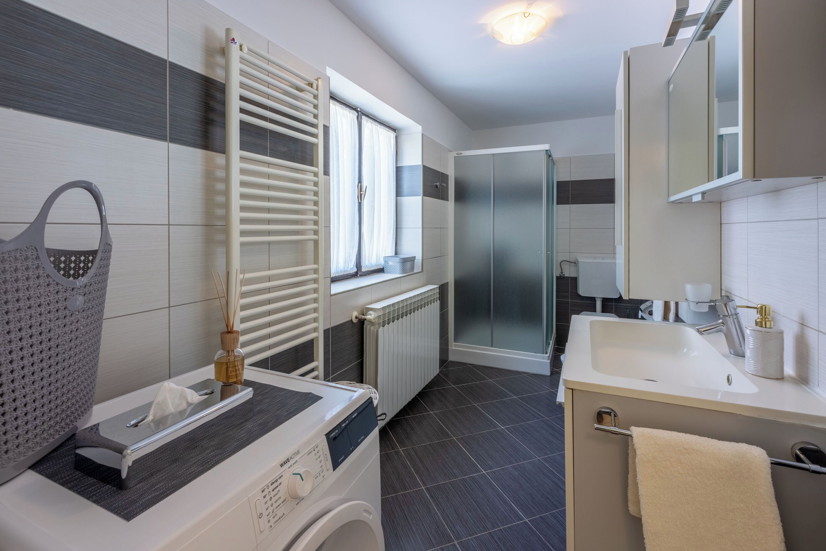 Une salle de bain moderne équipée d’un lave-linge intégré, d’un porte-serviettes, d’une cabine de douche en verre et d’un grand miroir.