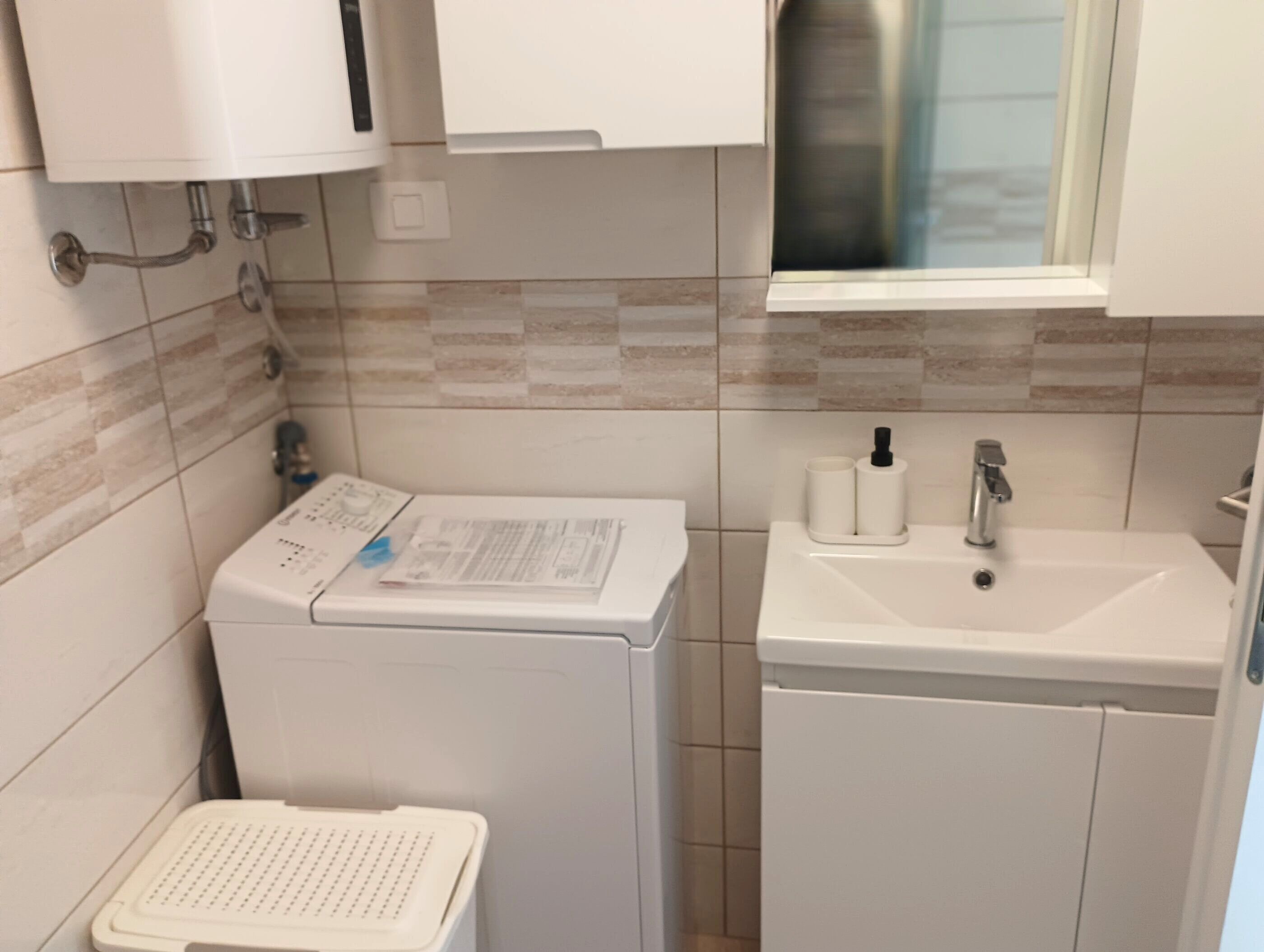 Ein kleines Badezimmer mit Waschmaschine, Waschbecken und kleinem Fenster.