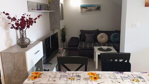 Ett kompakt vardagsrum med en soffa, ett litet bord, en tv och en vas med blommor.