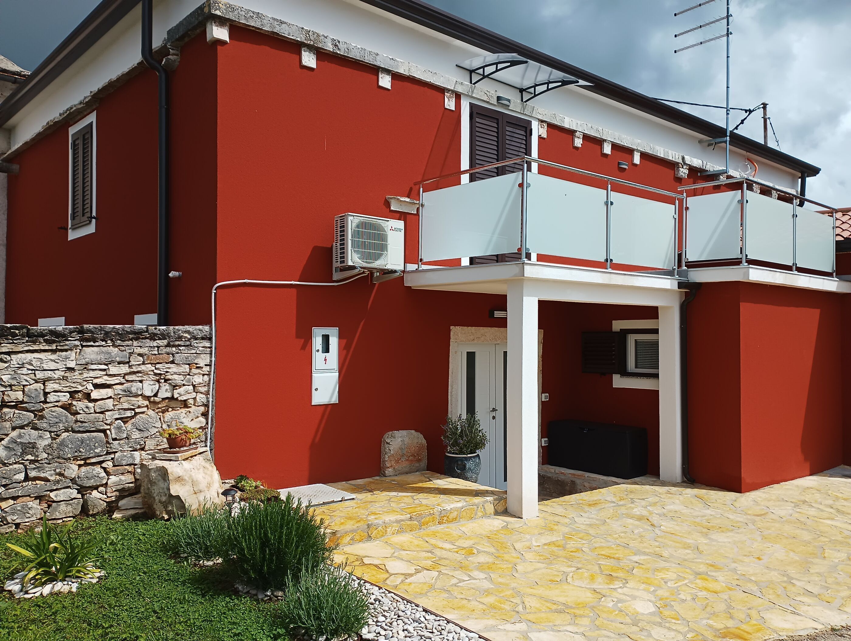 Ein rotes Gebäude mit einer Steinmauer, einem Balkon und einer Klimaanlage.