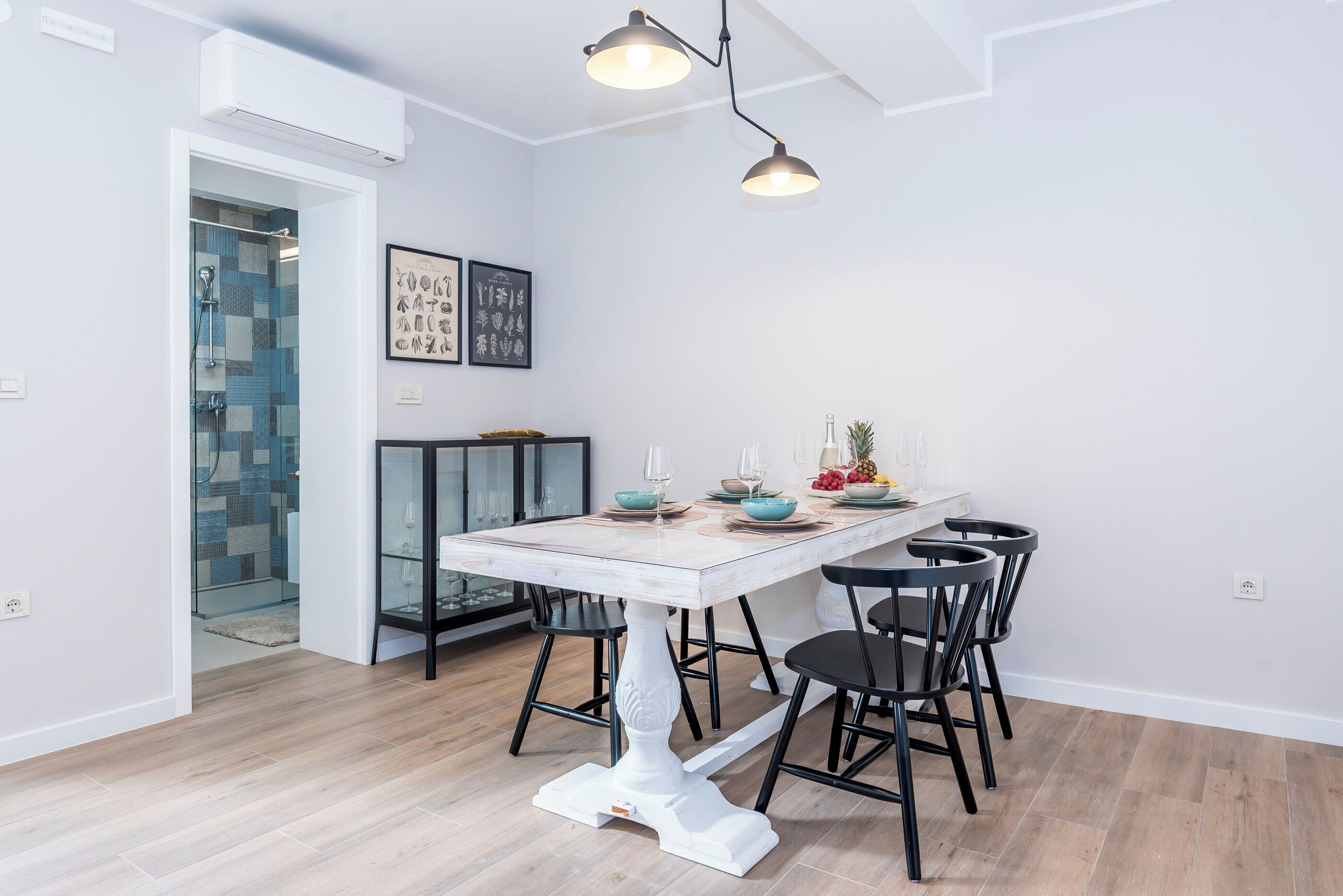 A modern dining area with a white table, black chairs, and pendant lighting.
