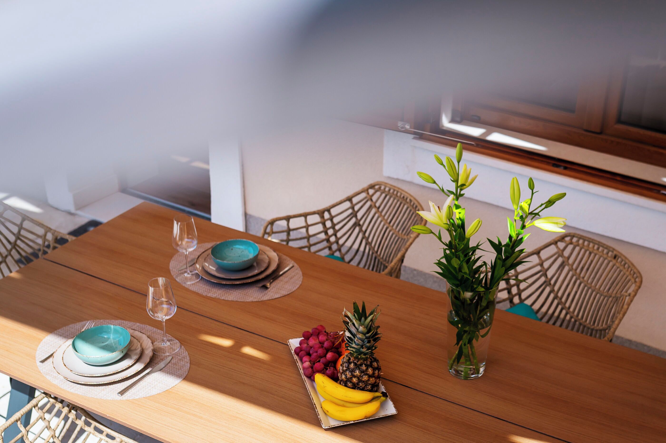 A dining table with a fruit arrangement, a vase with flowers, and a television in the background.