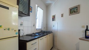 Une cuisine équipée d’un réfrigérateur, d’une cuisinière et de placards. On peut voir des aimants décoratifs sur le réfrigérateur, une fenêtre avec des stores et une bouteille sur le comptoir.