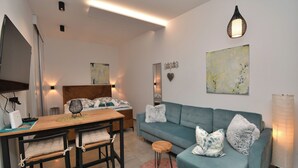 Uma sala de estar moderna com um sofá verde-água, uma mesa de jantar de madeira com duas cadeiras, um tapete rosa fofinho e um quadro abstrato grande na parede.
