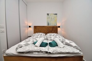 A neatly made bed with geometric patterned bedding, a wooden headboard, and a wall-mounted abstract painting. - Apartment Leprin (Labin)