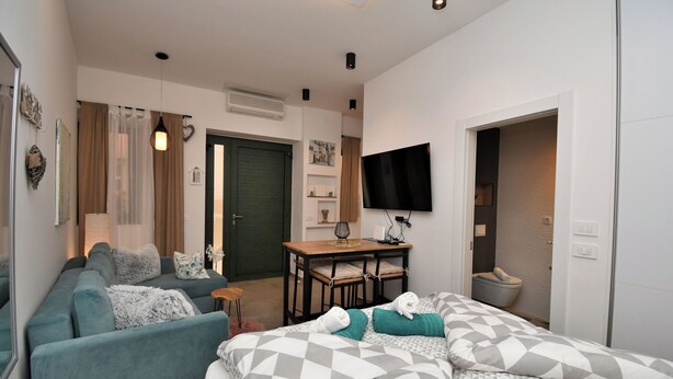 Quarto moderno com sofá, cama com roupa de cama estampada, escrivaninha com cadeira e televisão na parede.