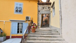 Degraus de pedra levam a um edifício amarelo com persianas azuis e um vaso de flores no patamar.