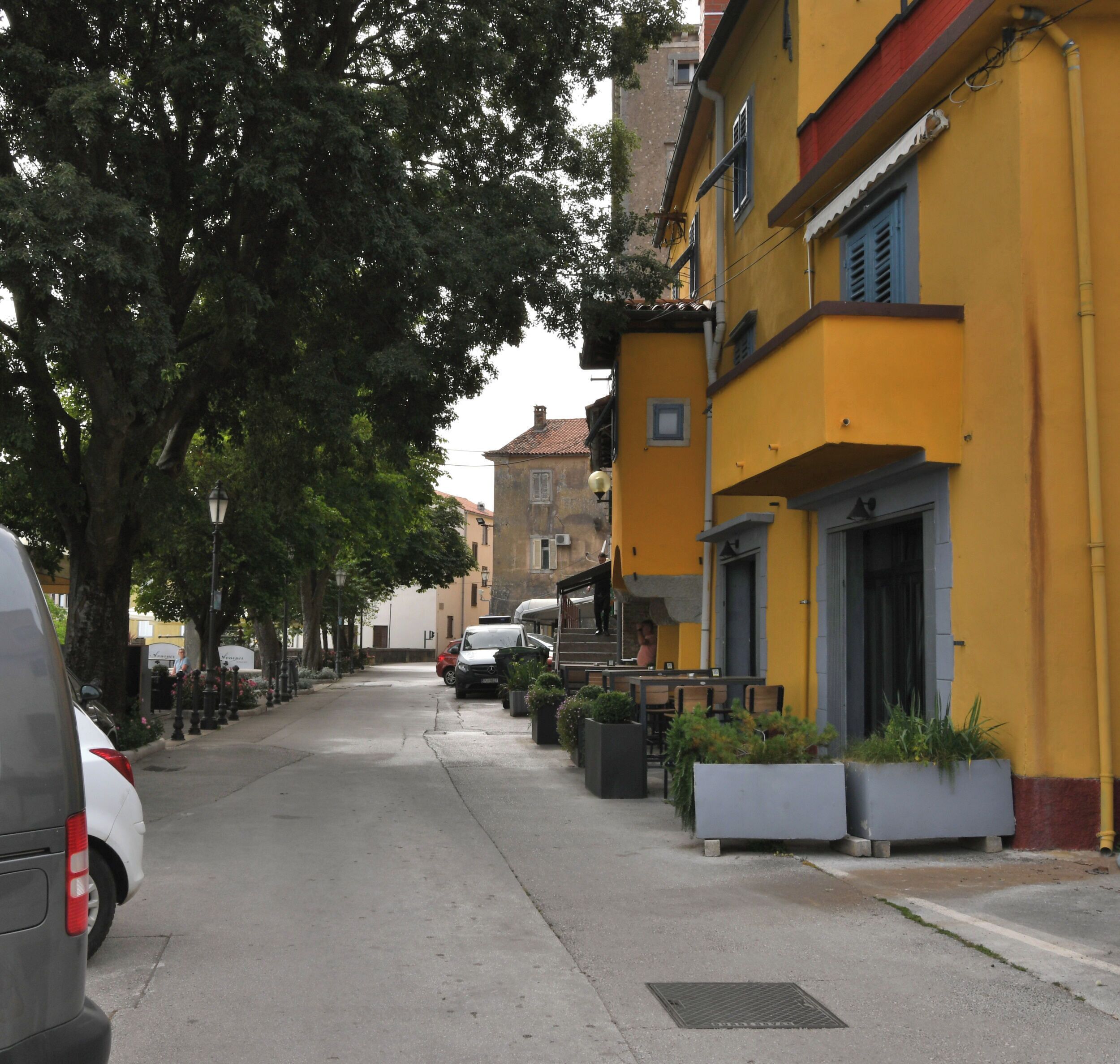 A street lined with yellow buildings, parked cars, and trees.