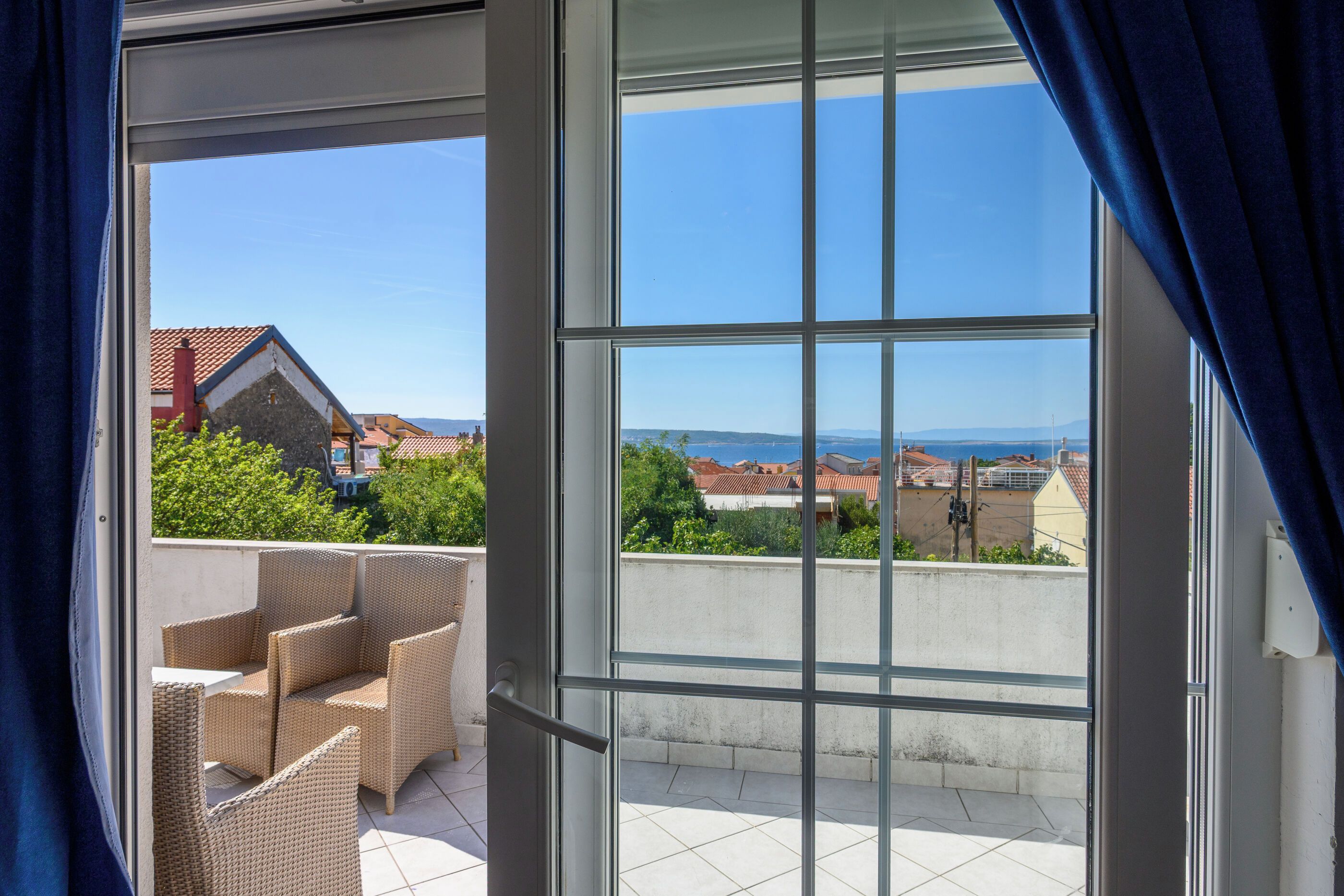 Een balkon met rieten meubels en een helder uitzicht op de omliggende gebouwen en het landschap.