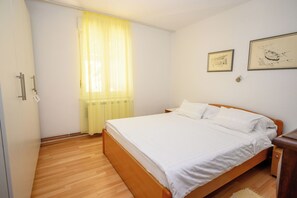 Een slaapkamer met een houten bed, een raam met gele gordijnen en twee ingelijste foto's aan de muur.