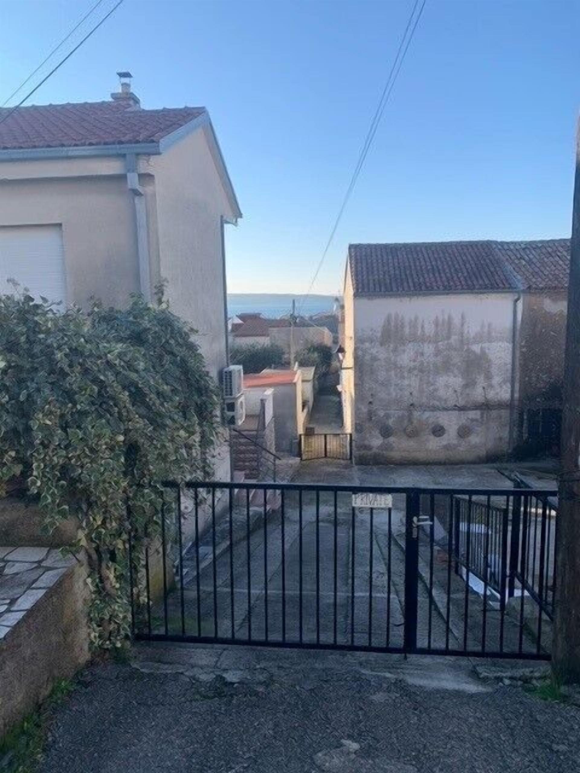 A gated courtyard with a building, a small structure, and a view of the sea.