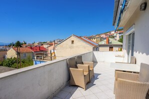 Een balkon met rieten meubilair, een zwembad en uitzicht op een stad met rode daken.