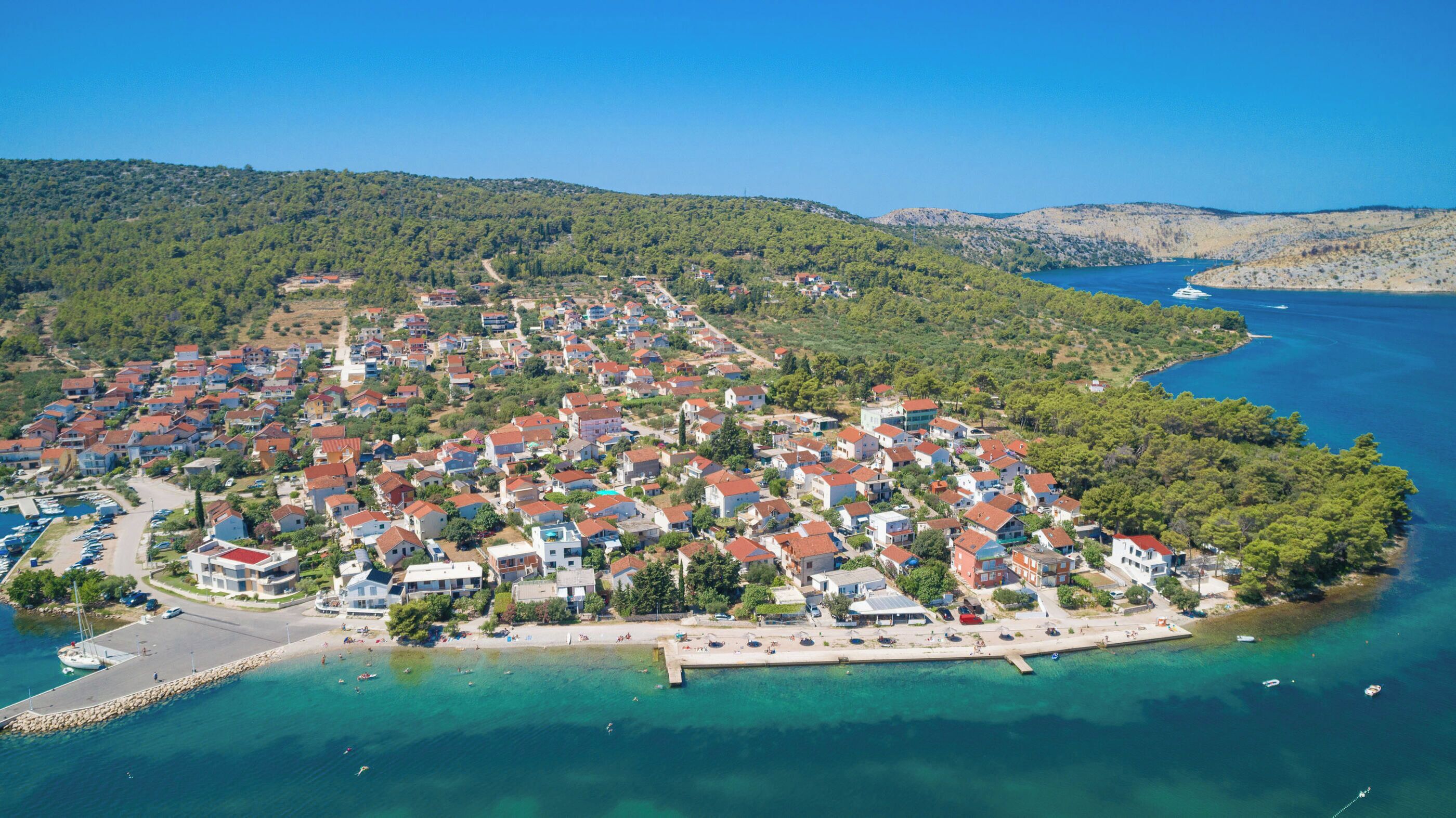 Vista aérea de uma área residencial costeira com casas, um porto de iates e um mar azul límpido.