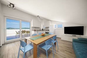 A modern, open-plan living space with a dining area, kitchen, and a large TV. - Apartments Picikato (Bilice)