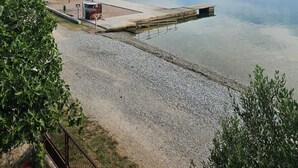 En rolig sø med en mole, der stikker ud i vandet, omgivet af grøn vegetation og en klar himmel.