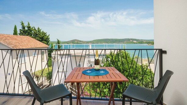 En balkon med et bord og to stole, udsigt over vand og grøn bevoksning.