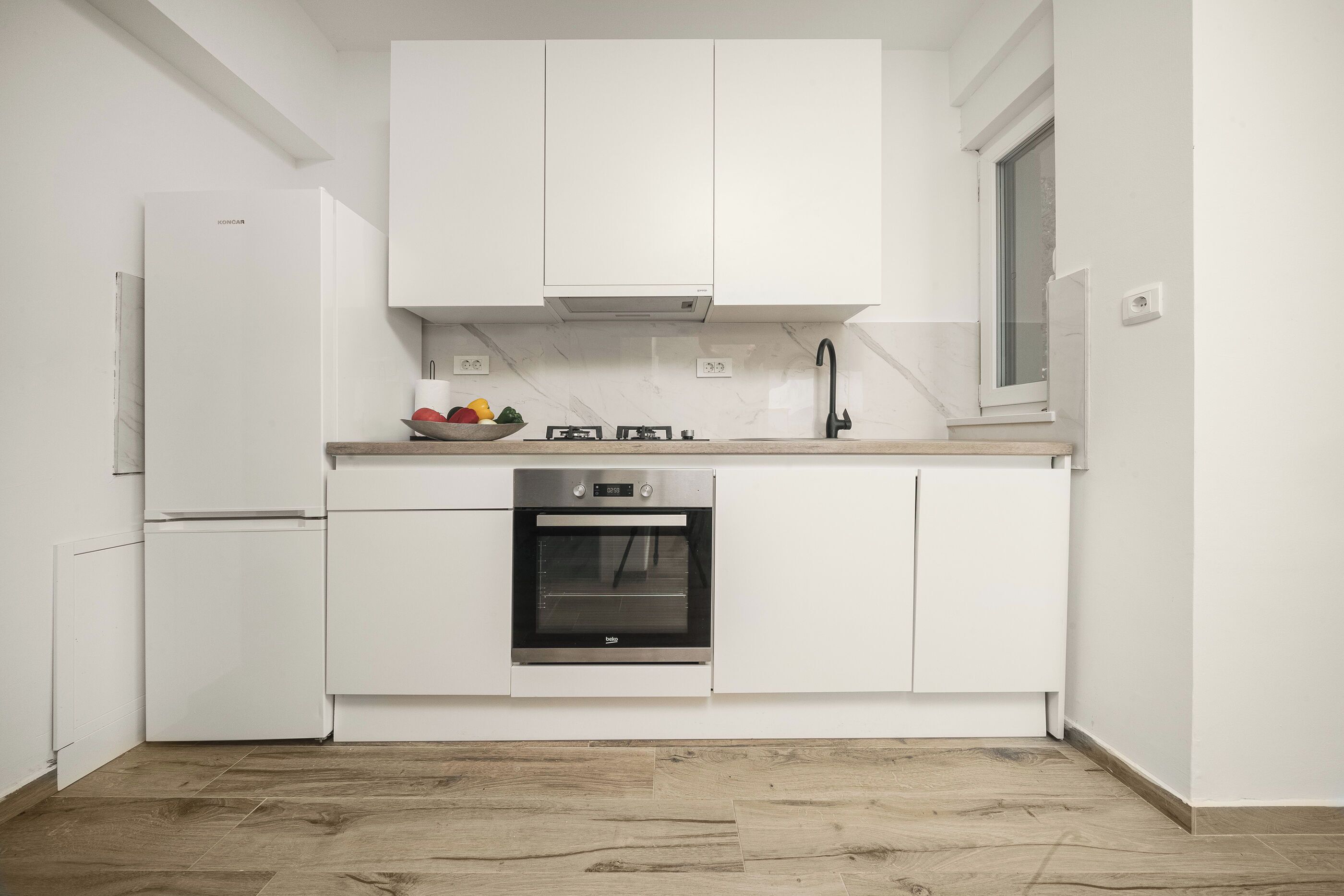 A modern kitchen with white cabinetry, a built-in oven, and a stainless steel refrigerator.