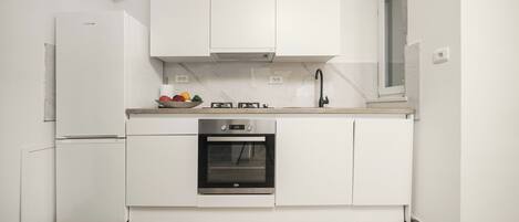A modern kitchen with white cabinetry, a built-in oven, and a stainless steel refrigerator.