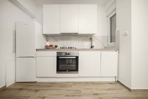 Une cuisine moderne avec des meubles blancs, un four encastré et un réfrigérateur en acier inoxydable.